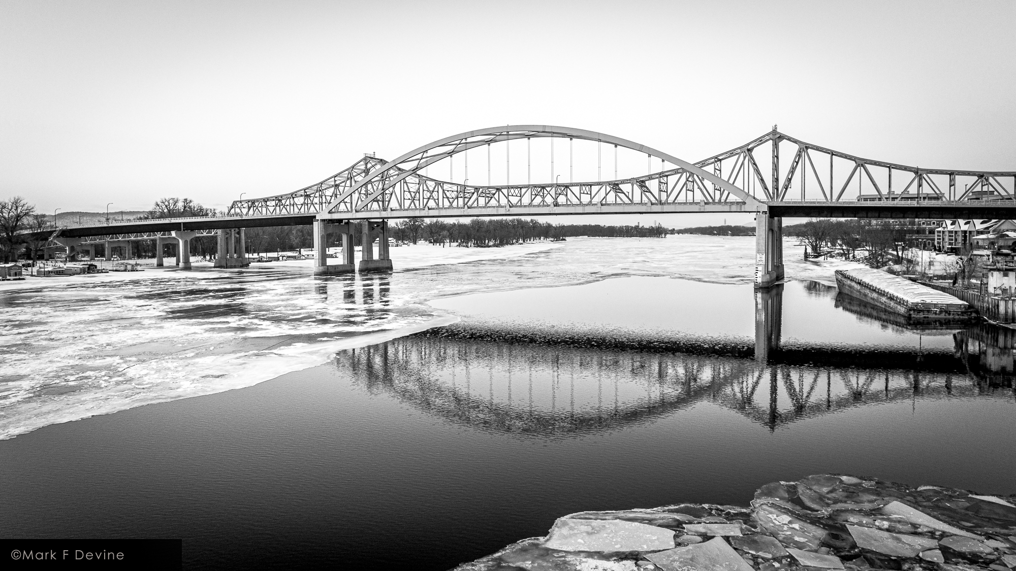 The bridges over the main channel of the Mississippi River in La Crosse, Wisconsin are reflected in a patch of open water. This...